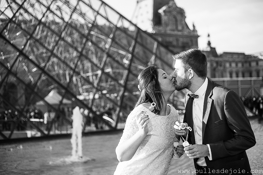 Couple s'embrassant devant la pyramide du Louvre | Bulles de Joie Photographie, photographe d'amoureux àParis
